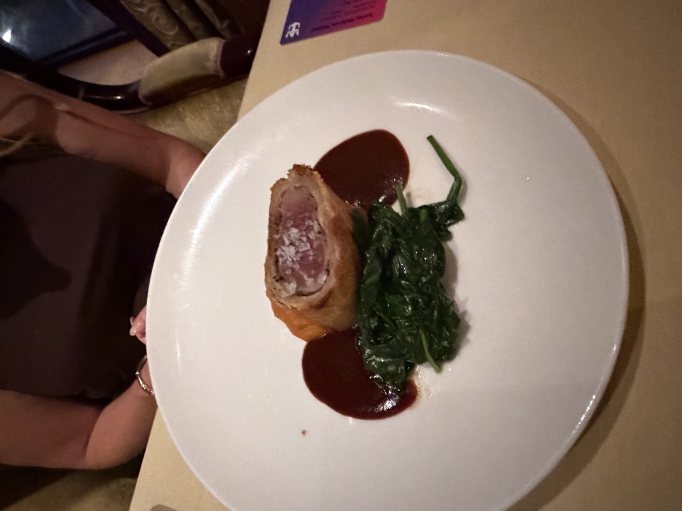 A slice of beef Wellington with sauteed spinach and red wine jus on a white plate