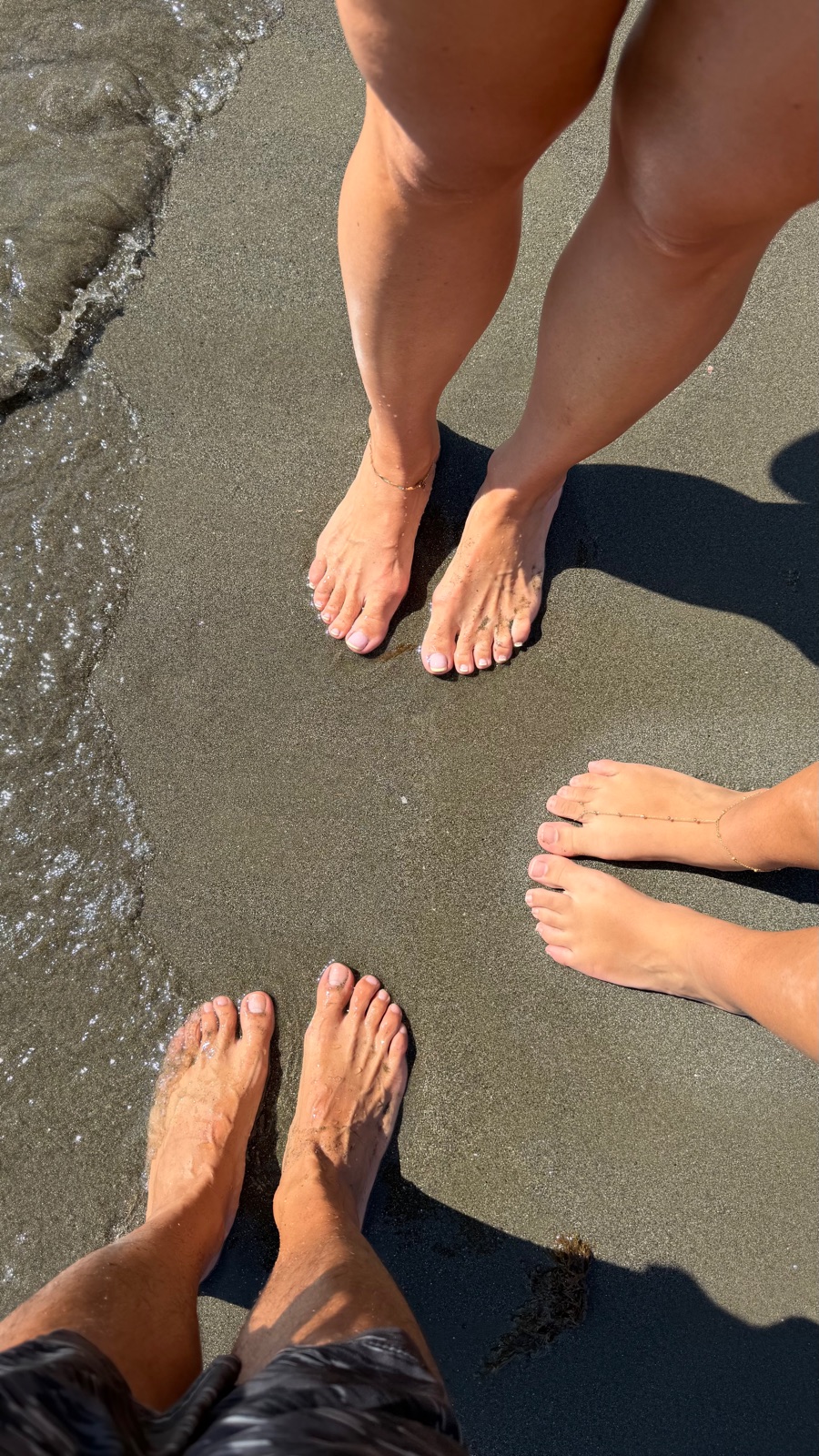 Three pairs of feet in the surf at the water's edge