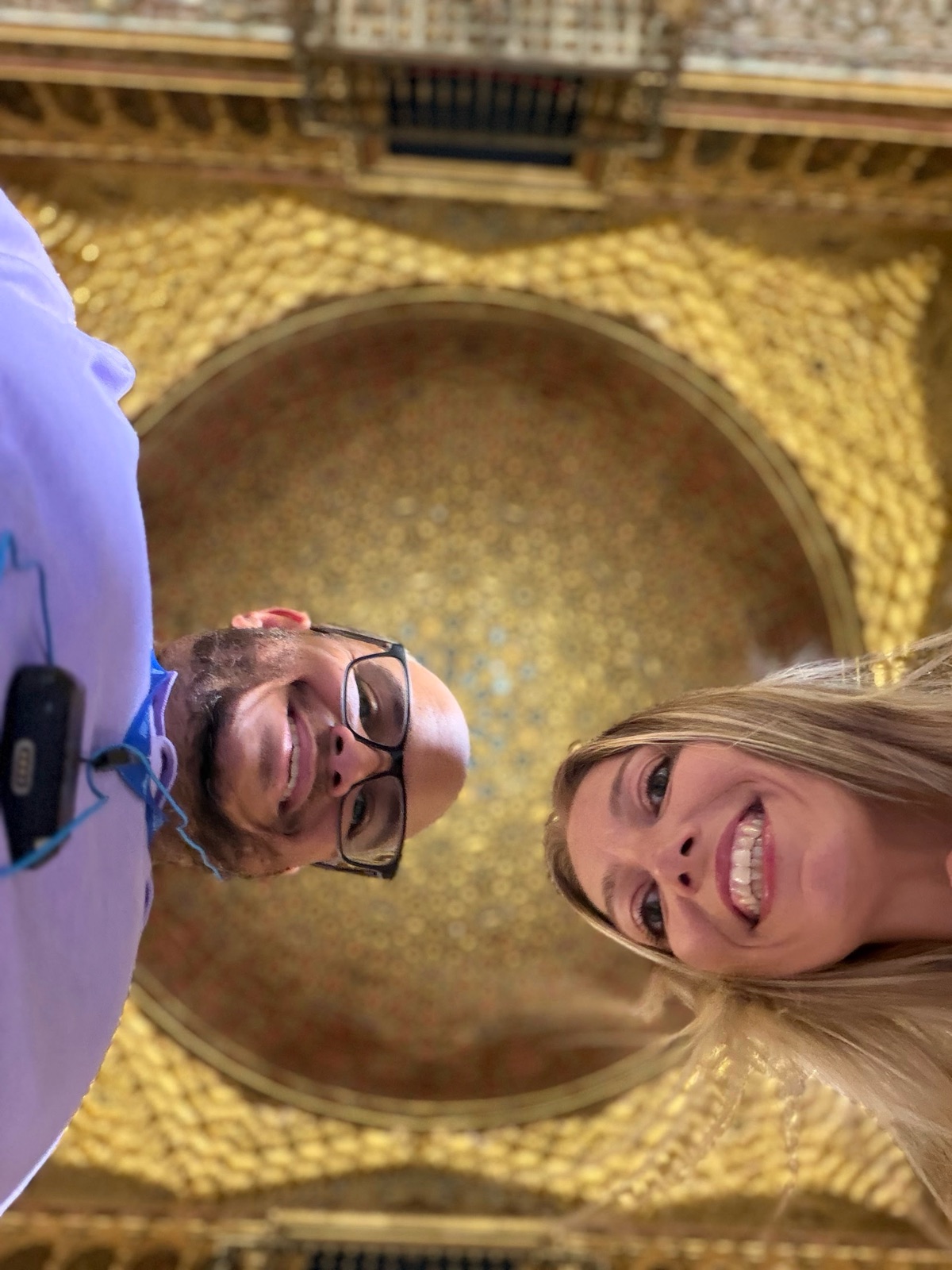 Miguel and Ashley under a gilded dome, wearing tour audio guides