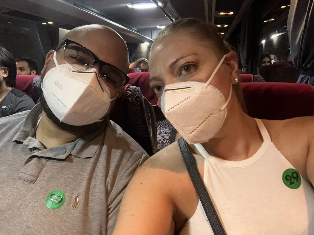 Miguel and Ashley in masks on a tour bus with green excursion stickers
