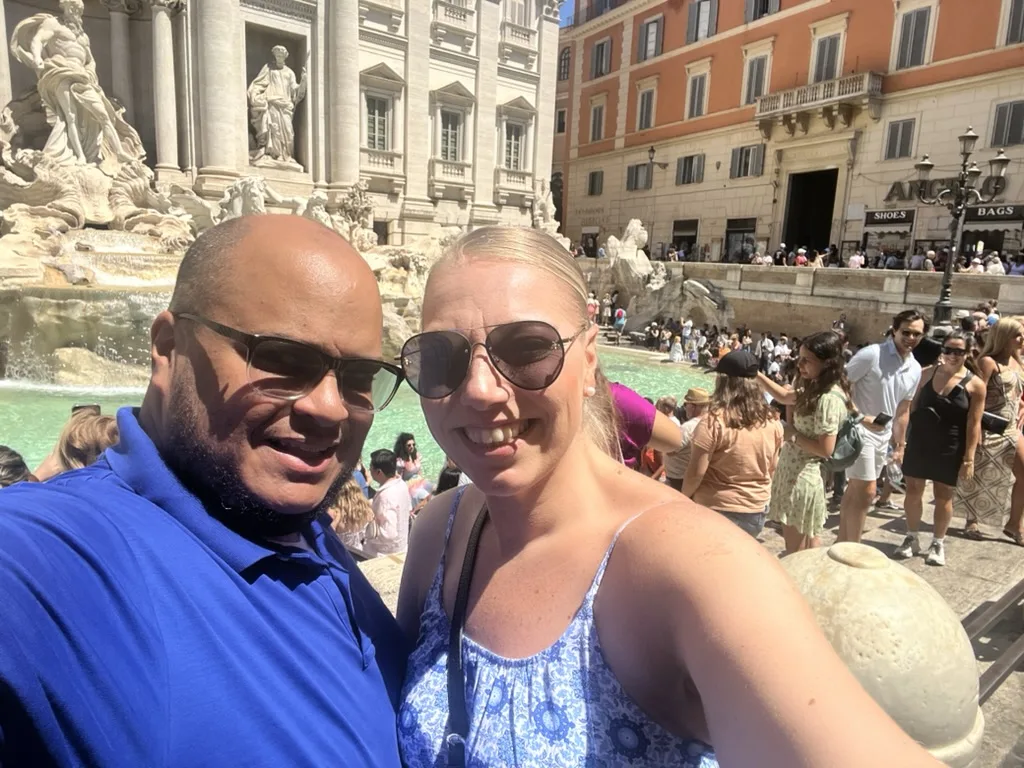 Miguel and Ashley taking a selfie at the Trevi Fountain with a crowd behind them